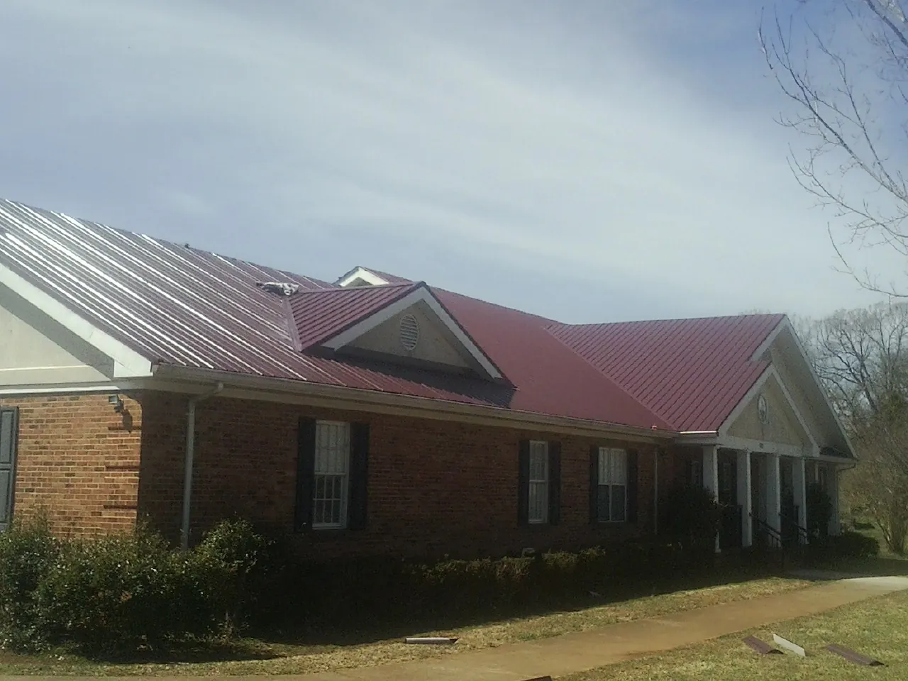 Red metal roof with gabled entries on a long brick building, from a Hail Damage Roof Repair job in Constantia